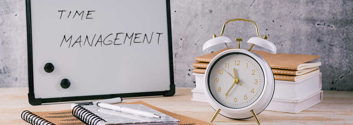 Time management written on a board beside a clock and notebooks
