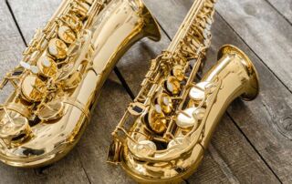 Close-up photograph of two saxophones placed on a wooden floor.