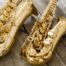 Close-up photograph of two saxophones placed on a wooden floor.