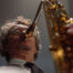 Professional saxophonist playing on stage with a close-up view of the instrument.