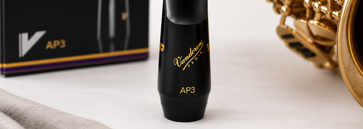Bec de saxophone alto Vandoren AP3 présenté aux côtés d’un saxophone et de sa boîte