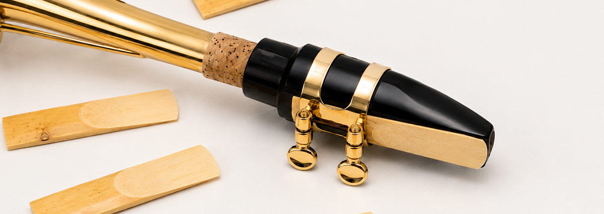 Bec de saxophone avec anche et ligature, présenté à côté d’anches seules